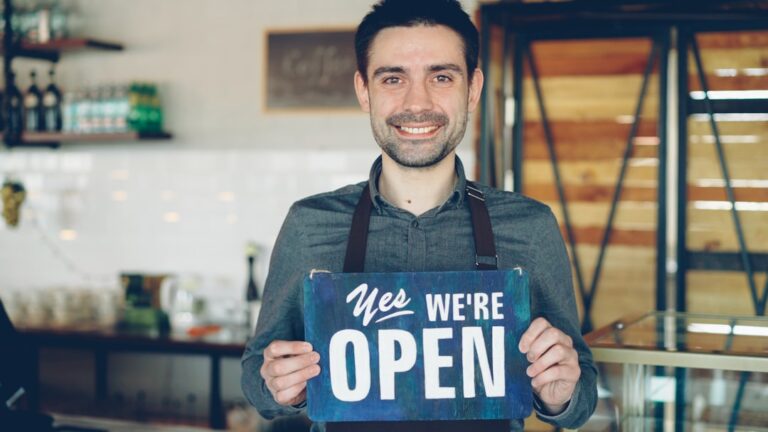 Barista holds an "open" sign, welcoming customers.