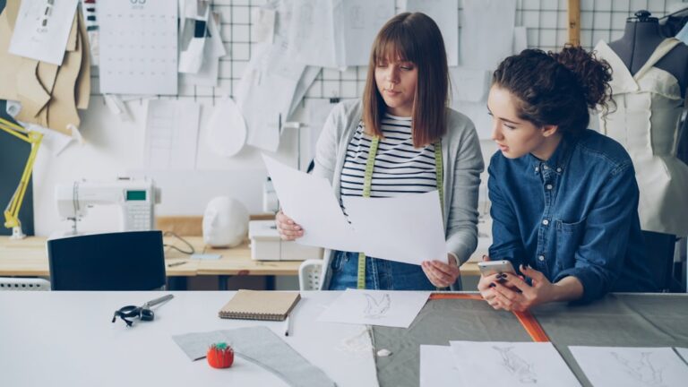 Two women discuss designs in a workshop.